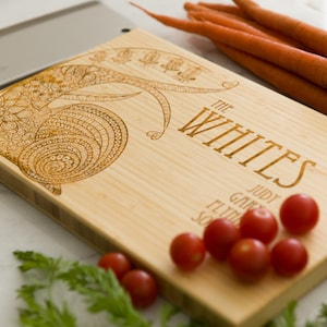 Puede incluir: Una tabla de cortar de bambú personalizada con un diseño intrincado y el texto "The Whites" grabado en la superficie. La tabla también presenta los nombres "Judy, Gary, Flynn y Sophia" grabados debajo del apellido.