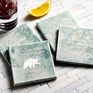 May include: Four green square coasters with white text and a bear graphic. The coasters feature the following text: "Bears probably don't even realize that we have a right to their arms." "I'm not as mean as I could be. I want people to be more grateful for that."  "Daughter" and "Wild Child, Chill Mom".