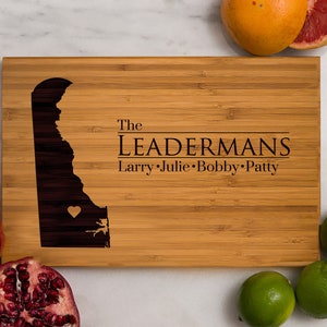 May include: A personalized bamboo cutting board with an outline of the state of Delaware and the text "The Leadermans Larry Julie Bobby Patty".