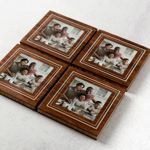 May include: Set of four wooden coasters with a photo of a family of five in a kitchen. The coasters have a brown wood frame with a white border around the photo.