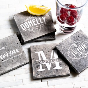 Puede incluir: Cuatro posavasos de piedra gris con letras blancas. Los posavasos presentan los nombres "Donnelly", "Emerson", "Marshall" y "Coleman Family".