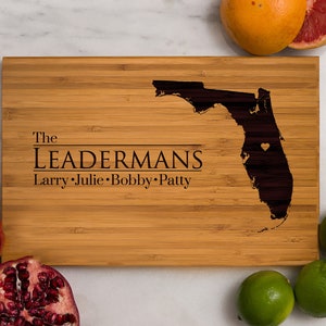 May include: A personalized bamboo cutting board with the text "The Leadermans Larry. Julie. Bobby. Patty" and a silhouette of the state of Florida with a heart in the center.