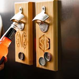 May include: Two wooden magnetic bottle openers with engraved initials. The opener on the left has the initials "NW" and the opener on the right has the initials "SG". Both openers have a silver bottle opener attached to the wood.