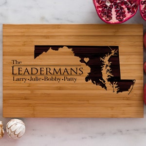 May include: A personalized bamboo cutting board with an engraved outline of the state of Maryland, including a small heart in the center. The text "The Leadermans Larry.Julie.Bobby.Patty" is engraved below the state outline.