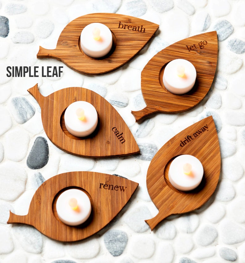Op de afbeelding: Vijf houten, bladvormige kaarshouders met de woorden "breath", "let go", "calm", "drift away" en "renew" erin gegraveerd. Elke houder heeft een kleine, ronde inkeping voor een theelichtje.