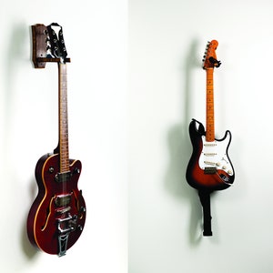 Puede incluir: Dos guitarras eléctricas colgadas en soportes de pared. La guitarra de la izquierda es una guitarra de cuerpo hueco con un acabado rojo oscuro. La guitarra de la derecha es una guitarra de cuerpo sólido con un acabado sunburst.