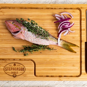 May include: A bamboo cutting board with a knife holder, a whole fish, red onion slices, and the text "EST. 2020 STEPHENSON FAMILY" engraved on the surface.