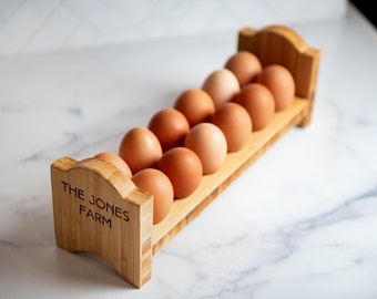 Puede incluir: Un soporte de huevos de madera con el texto "THE JONES FARM" grabado en el lateral. El soporte está lleno de una docena de huevos marrones.