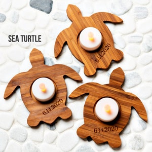 Op de afbeelding: Drie houten zeeschildpad kaarshouders met een theelichtje in elk. De houders zijn gegraveerd met de datum "6.14.2020".