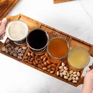 May include: A wooden serving tray with four small glasses filled with different types of beer. The tray also has four compartments filled with almonds, pistachios, and other snacks. The tray is engraved with the name "Richard".