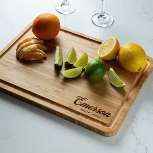 May include: A personalized bamboo cutting board with the names "Emerson", "Adalyn", and "Josiah" engraved on it. The board is surrounded by sliced oranges and limes.