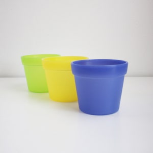 May include: Three plastic pots in different colours: green, yellow, and blue. The pots are all the same size and shape.