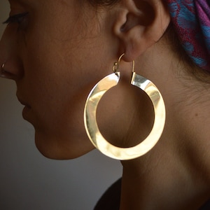 May include: A person wearing large, round, gold hoop earrings. The earrings are thick and have a hammered texture.