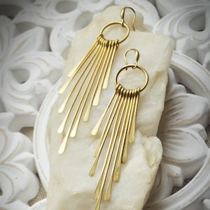 May include: A pair of gold dangle earrings with a circle design at the top and multiple thin, straight pieces of metal hanging down from the circle.