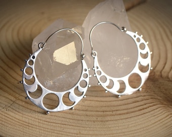 May include: A pair of silver hoop earrings with a crescent moon design. The earrings are made of metal and have a delicate, intricate design.
