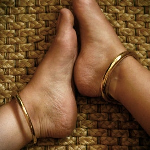 May include: Two bare feet with gold anklets on a woven straw mat.