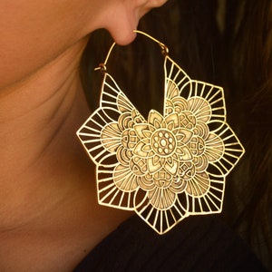 K&ouml;nnte beinhalten: Goldfarbene gro&szlig;e Creolen mit einem detaillierten Mandala-Design. Die Ohrringe sind aus Metall und haben ein filigranes, kompliziertes Muster.