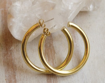 May include: A pair of gold hoop earrings. The earrings are thick and have a simple, modern design.