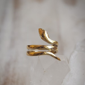 May include: A gold-toned snake ring with a textured finish. The ring is wrapped around a white crystal.
