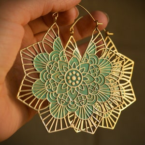 K&ouml;nnte beinhalten: Ein Paar goldene Creolen mit einem t&uuml;rkisfarbenen Mandala-Design. Die Ohrringe sind gro&szlig; und filigran, mit einem zarten, durchbrochenen Design.