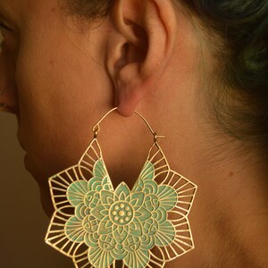 K&ouml;nnte beinhalten: Ein Paar gro&szlig;e goldene Creolen mit einem t&uuml;rkisfarbenen Mandala-Design. Die Ohrringe sind aus Metall und haben ein filigranes, kompliziertes Muster.