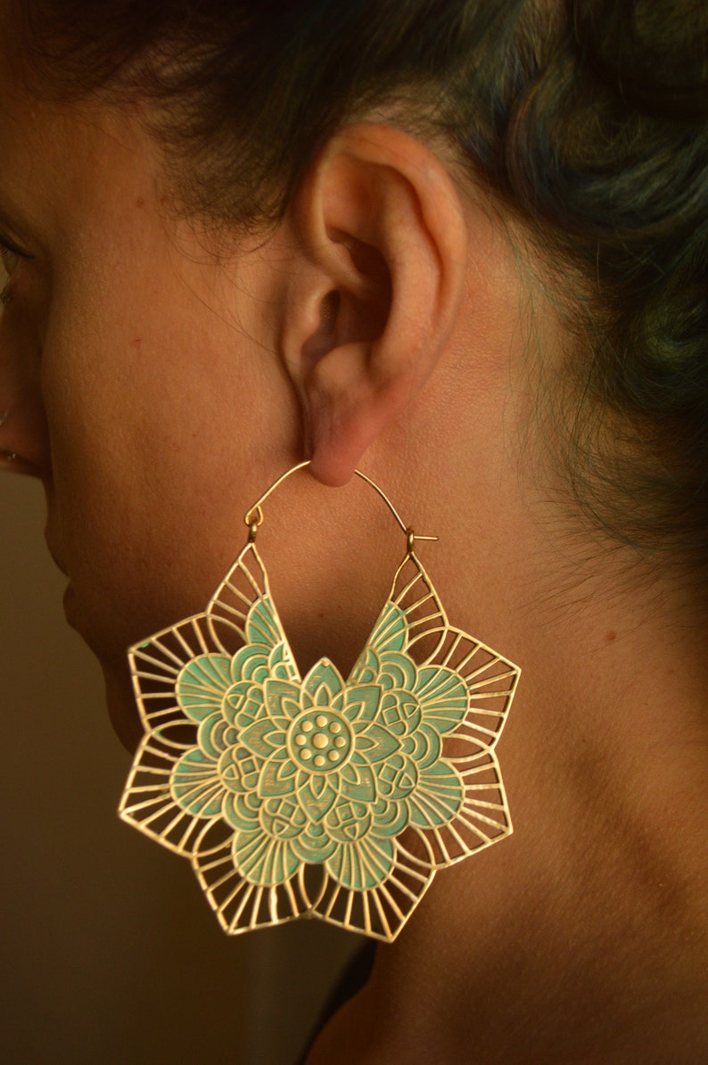 K&ouml;nnte beinhalten: Ein Paar gro&szlig;e goldene Creolen mit einem t&uuml;rkisfarbenen Mandala-Design. Die Ohrringe sind aus Metall und haben ein filigranes, kompliziertes Muster.