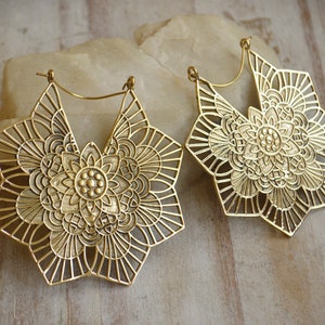 K&ouml;nnte beinhalten: Ein Paar gro&szlig;e, goldfarbene, durchbrochene Ohrringe mit einem Mandala-Design. Die Ohrringe sind sternf&ouml;rmig mit filigranen Details.