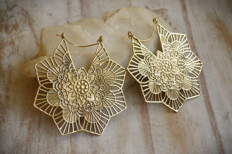 K&ouml;nnte beinhalten: Ein Paar gro&szlig;e, goldfarbene, durchbrochene Ohrringe mit einem Mandala-Design. Die Ohrringe sind sternf&ouml;rmig mit filigranen Details.