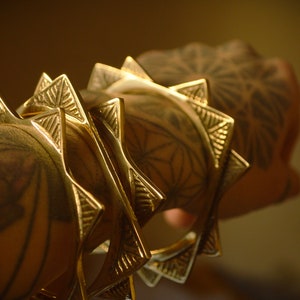 May include: Four gold-toned metal bracelets with a geometric, starburst design. Each bracelet has a series of pointed edges.