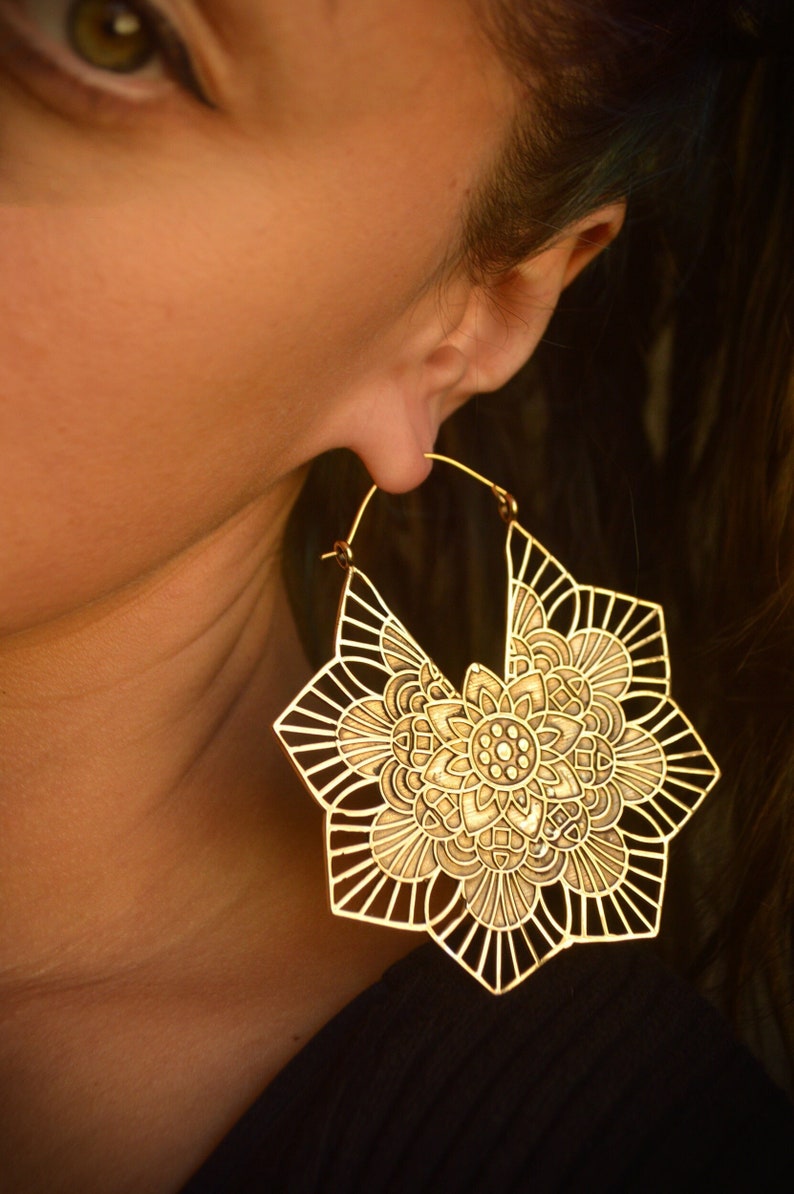 K&ouml;nnte beinhalten: Goldfarbene gro&szlig;e Creolen mit einem detaillierten Mandala-Design. Die Ohrringe sind aus Metall und haben ein filigranes, kompliziertes Muster.