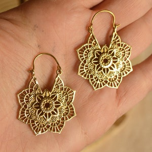 K&ouml;nnte beinhalten: Ein Paar goldfarbene Ohrringe mit einem floralen Mandala-Design. Die Ohrringe haben einen Klappverschluss und bestehen aus einem gl&auml;nzenden, metallischen Material. Das filigrane Openwork-Design zeigt eine zentrale Blume und umliegende Bl&uuml;tenbl&auml;tter.