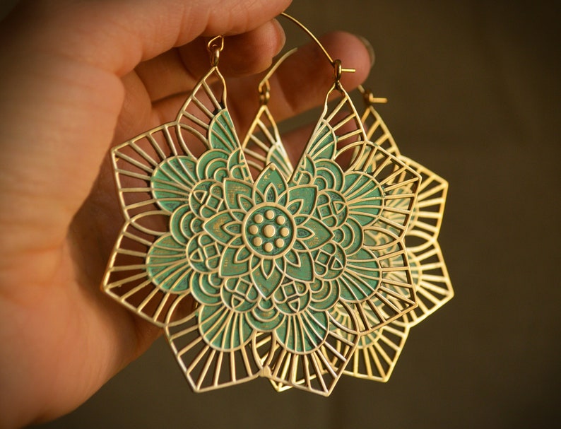 K&ouml;nnte beinhalten: Ein Paar goldene Creolen mit einem t&uuml;rkisfarbenen Mandala-Design. Die Ohrringe sind gro&szlig; und filigran, mit einem zarten, durchbrochenen Design.