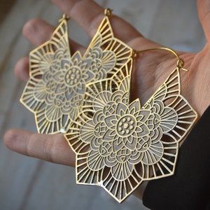 K&ouml;nnte beinhalten: Ein Paar gro&szlig;e, goldfarbene Ohrringe mit einem detaillierten Mandala-Design. Die Ohrringe sind aus Metall und haben einen B&uuml;gelverschluss.