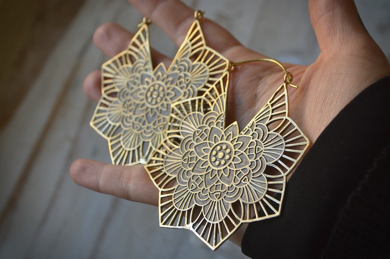 K&ouml;nnte beinhalten: Ein Paar gro&szlig;e, goldfarbene Ohrringe mit einem detaillierten Mandala-Design. Die Ohrringe sind aus Metall und haben einen B&uuml;gelverschluss.