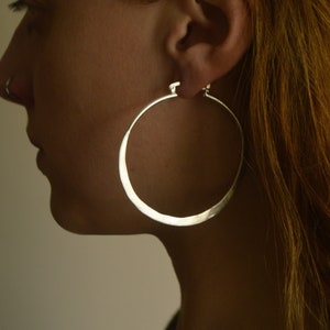 May include: A person wearing large, silver hoop earrings. The earrings are thick and have a slightly hammered finish.