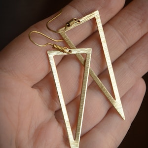May include: A pair of gold triangle earrings with a brushed finish. The earrings are simple and modern in design.