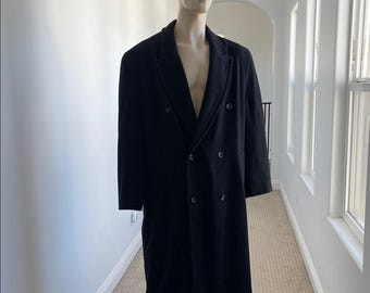 Puede incluir: Un abrigo negro de doble botonadura con solapas y seis botones. El abrigo se exhibe en un maniquí en un pasillo con paredes y ventanas blancas.
