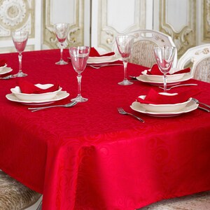 Könnte beinhalten: Eine rote Tischdecke mit Damastmuster ist für ein formelles Abendessen gedeckt. Der Tisch ist mit weißen Tellern, roten Servietten und klaren Glaskelchen gedeckt.