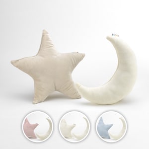 Può includere: Un cuscino a forma di stella beige e un cuscino a forma di mezzaluna bianco sono esposti su uno sfondo bianco. I cuscini sono morbidi e soffici. Tre immagini circolari più piccole mostrano i cuscini a forma di luna e stella in rosa, bianco e blu.