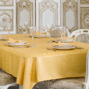 May include: A yellow tablecloth with a swirl pattern, set for a formal dinner with white plates, silverware, and wine glasses.