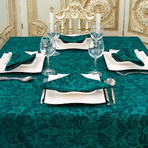 Könnte beinhalten: Eine grüne Tischdecke mit Damastmuster ist für ein formelles Abendessen gedeckt. Der Tisch ist mit weißen Tellern, grünen Servietten und klaren Weingläsern gedeckt.