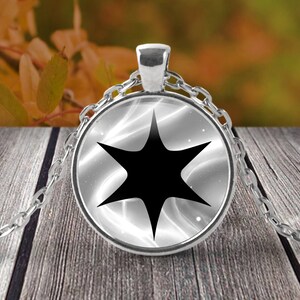 May include: A silver chain necklace with a round glass pendant featuring a black starburst design on a white background.