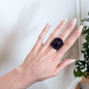 May include: A black ring with a large oval-shaped black stone set in a rose-shaped design.