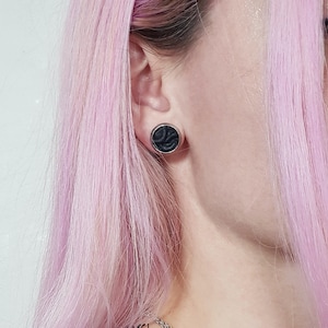 May include: A person with pink hair wearing black lace earrings and a black lace top with a silver chain necklace.