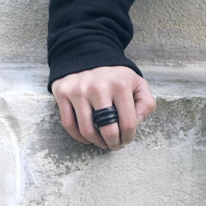 May include: A black ring with a ridged design. The ring is worn on the middle finger of a hand.