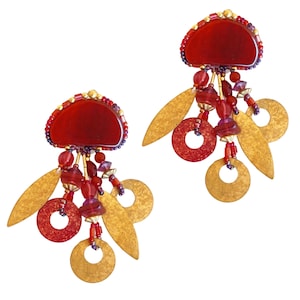 May include: A pair of statement earrings featuring a half-circle of deep red material, adorned with small beads. Gold-colored leaf and circular shapes dangle below, along with strands of red and purple beads. The earrings have a unique, artistic design.