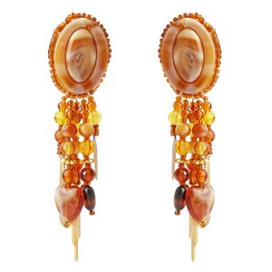 May include: A pair of dangle earrings featuring oval-shaped amber-colored resin tops with beaded trim. The earrings have strands of yellow, orange, and brown beads, with heart-shaped pendants and gold-colored fringe.