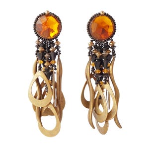 May include: A pair of dangling earrings with a large, amber-colored gemstone at the top. The earrings feature a mix of black, gold, and amber beads, with gold-toned teardrop and elongated shapes hanging below. The earrings have a vintage or bohemian style.