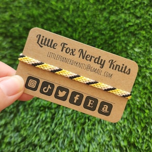 May include: A brown card with the text "Little Fox Nerdy Knits" and the email address "littlefoxnerdyknits@gmail.com". The card has a black, yellow, and white friendship bracelet on it. There are social media icons for Instagram, TikTok, Twitter, Facebook, Etsy, and Amazon.