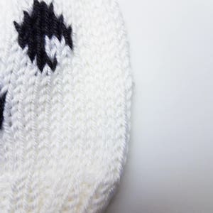 May include: White knitted hat with black and white polka dots. The hat is made of a soft, textured yarn.